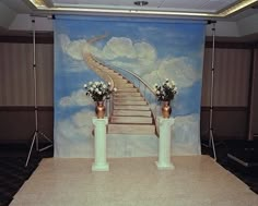 an empty stage set up for a wedding with flowers on the steps and clouds painted on the wall