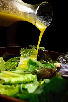 someone pouring dressing onto a salad in a bowl