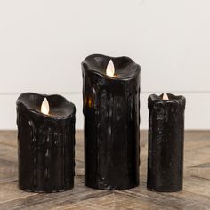 three black candles sitting on top of a wooden table