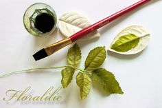 a brush and some leaves on a white surface with the word floralie written in gold