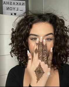 a woman holding her hands up to her face with hendi tattoos on it's palms