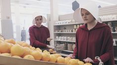 two women in red shirts and white hats are shopping for oranges