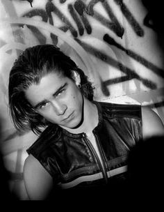 black and white photograph of a young man in front of graffiti on a wall with his head tilted to the side