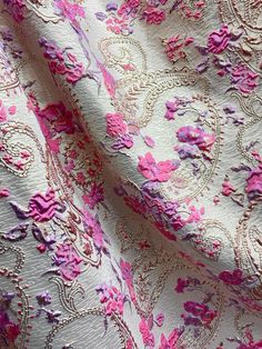 a pink and purple fabric with flowers on it's side, in the middle of an intricate pattern