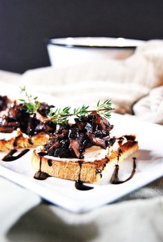 two pieces of bread topped with mushrooms and sauce on top of a white square plate