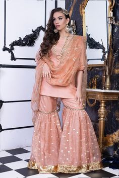 "Jolie Pastels are created for gharara and it can be clearly observed in the beautifully crafted \"Jolie\". Pastel hued bridal couture has been in hype for quite some time, and they aren't going out of fashion for long. Jolie has been crafted in salmon peach silk blouse with round neck and ¾ sleeves. The back of the blouse has been adorned with beautifully matched rope and beads tassels. The flowy gharara pants is a double layered silk and organza piece with gold foil lace and elegant silk dori work on both borders. Paired with flowy organza net dupatta adorned with silk dori work, sequins and tilla embroidery. This dress is perfect for nikah brides, engagement brides, bridesmaids, and all the festive occasions. Top: Color: Peach Fabric: Pure silk Gota edge finish ¾ sleeves Back contains d Gharara Pants, Beads Tassels, Salmon Peach, Engagement Bride, Sister Wedding, Net Dupatta, Formal Attire, Bridal Couture, Buy Dress