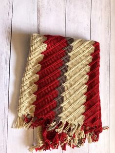 a red, beige and brown blanket laying on top of a white wooden floor next to a wall