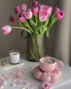 pink tulips in a vase on a white table with petals scattered around it