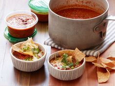 three bowls of chili, tortilla chips and salsa on a wooden table next to a pot