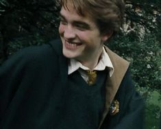 a young man wearing a harry potter sweater and smiling at the camera with trees in the background