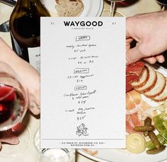 two people are holding up a menu at a table full of food and wine glasses