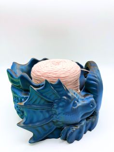 a blue ceramic bowl with a pink yarn ball in the center and two dragon heads on it