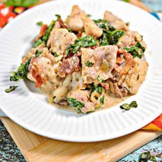 a white plate topped with chicken and spinach covered in sauce on top of a wooden cutting board