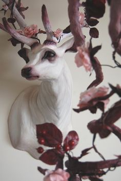 a white deer with antlers and flowers on it's head hanging from a branch