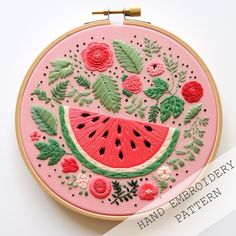 a watermelon embroidered onto a pink hoop with flowers and leaves around it, on a white surface