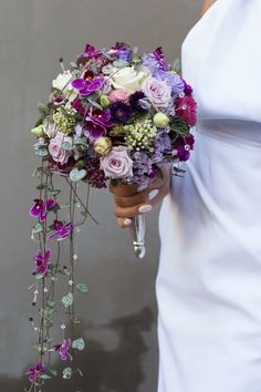 a woman holding a bouquet of flowers in her hand and wearing a white dress with purple accents