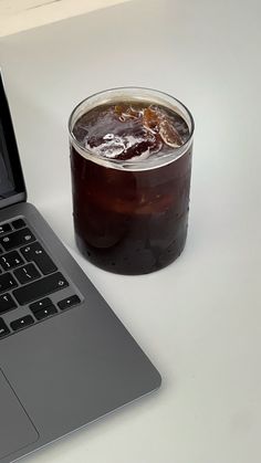 an open laptop computer sitting on top of a white table next to a cup of soda