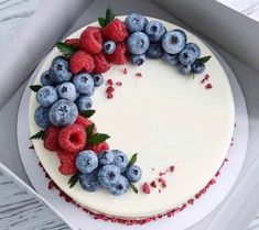 a cake decorated with berries and blueberries in a white box on a wooden table