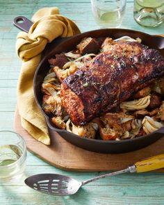 a pan filled with meat and onions on top of a wooden table next to a glass of water