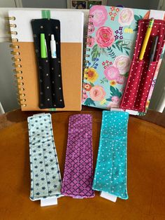 four notebooks lined up next to each other on top of a wooden table with pens and paper