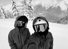 two snowboarders pose for the camera in front of snowy mountains