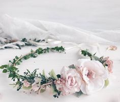 a flower crown with pink flowers and greenery around it on a white tablecloth