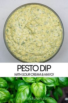 pesto dip with sour cream and mayo in a glass bowl next to basil leaves