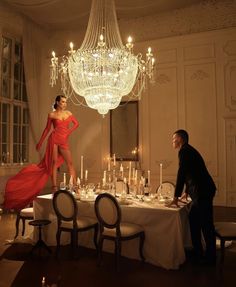 a man standing next to a table with a woman in a red dress on it