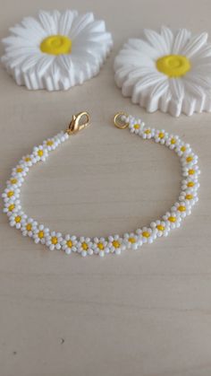 three white and yellow beaded bracelets sitting on top of a table next to flowers