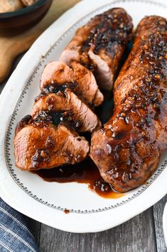 two pieces of meat sitting on top of a white plate covered in bbq sauce