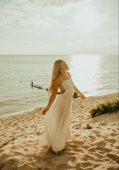 a woman standing on top of a sandy beach next to the ocean wearing a white dress