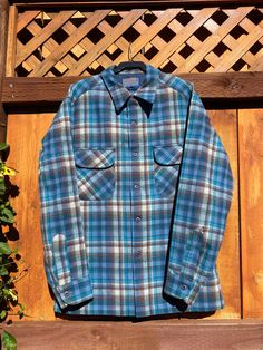 This is a vintage Pendleton brand board shirt from the 60s or 70s. Classic blue and red plaid design. This shirt features a loop collar and flap chest pockets. This is in good vintage condition. There are a few pinholes and snags as pictured. This is tagged as a size medium. Please refer to measurements for best fit: Chest (pit-to-pit): 22.25" Shoulder-to-shoulder: 18" Length (collar-to-hem at back): 28.5" Sleeve (shoulder-to-cuff): 22.75" *all items are sold as-is. Feel free to contact with further questions. Retro Blue Shirt For Fall, Vintage Blue Shirt For Fall, Vintage Blue Flannel Shirt For Fall, Retro Collared Flannel Shirt With Pockets, Vintage Blue Shirt With Pockets, Retro Collared Flannel Shirt With Button Closure, Retro Collared Flannel Shirt, Vintage Plaid Collared Shirt, Vintage Collared Flannel Shirt With Button Closure