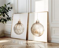 two framed christmas ornaments are hanging on the wall next to a potted green plant