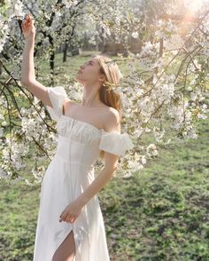 a woman in a white dress standing under a tree with flowers on it's branches