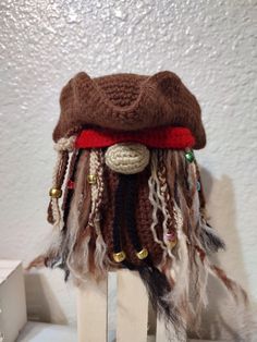 a brown hat with feathers and beads on top of a wooden stand in front of a white wall