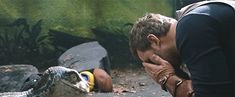 a man holding his head in front of an alligator that is laying on the ground