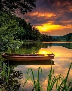 a boat sitting on top of a lake under a cloudy sky with the sun setting