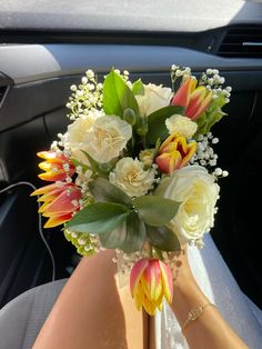 a vase filled with white and yellow flowers on top of a car dash board holder