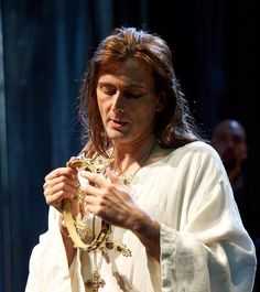 a man with long hair wearing a white robe and holding a snake in his hands