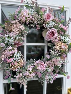 a wreath with pink flowers and greenery hanging on a window sill