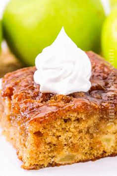 a piece of cake with whipped cream on top and two green apples in the background