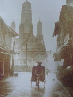 a man riding a bike down a street next to tall buildings in the rain with an umbrella over his head