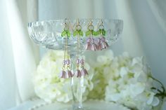 three pairs of pink and green earrings sitting on top of a glass stand next to white flowers