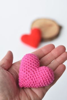 a small pink crocheted heart sitting in someone's hand next to some cookies