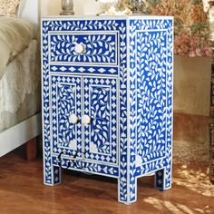 a blue and white cabinet sitting on top of a wooden floor next to a bed