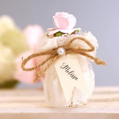 a small white jar with a pink flower on it and a name tag attached to it