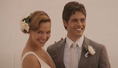 a man and woman standing next to each other in front of a white wall smiling at the camera