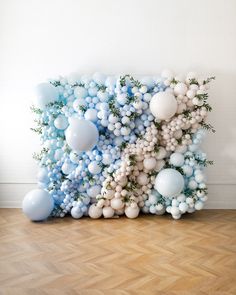 an arrangement of balloons and greenery is displayed on the floor in front of a white wall