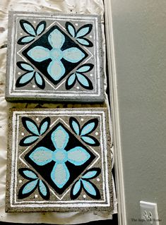 two blue and black tiles sitting on top of a white sheet covered floor next to a wall