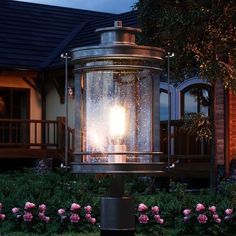 a light that is sitting on top of a post in front of some bushes and flowers